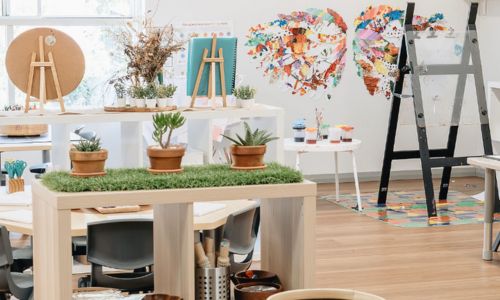 An indoor studio space with timber easels, potted plants and children's collage artwork on the wall.