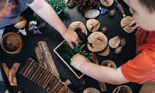 A child arranging timber rounds, bark and natural loose parts on a dark exploration table.