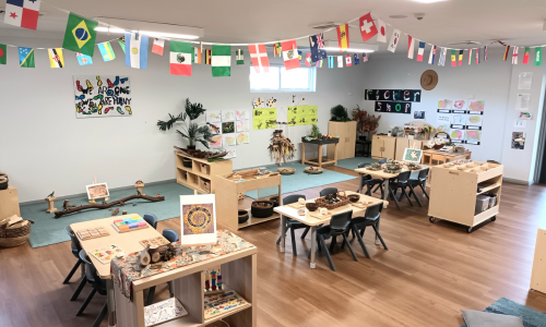 A classroom decorated with world flag bunting above tables set with natural materials and puzzles.