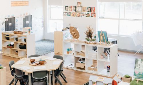 The preschool room with hexagonal tables, open timber shelving and children's work displayed on the walls.